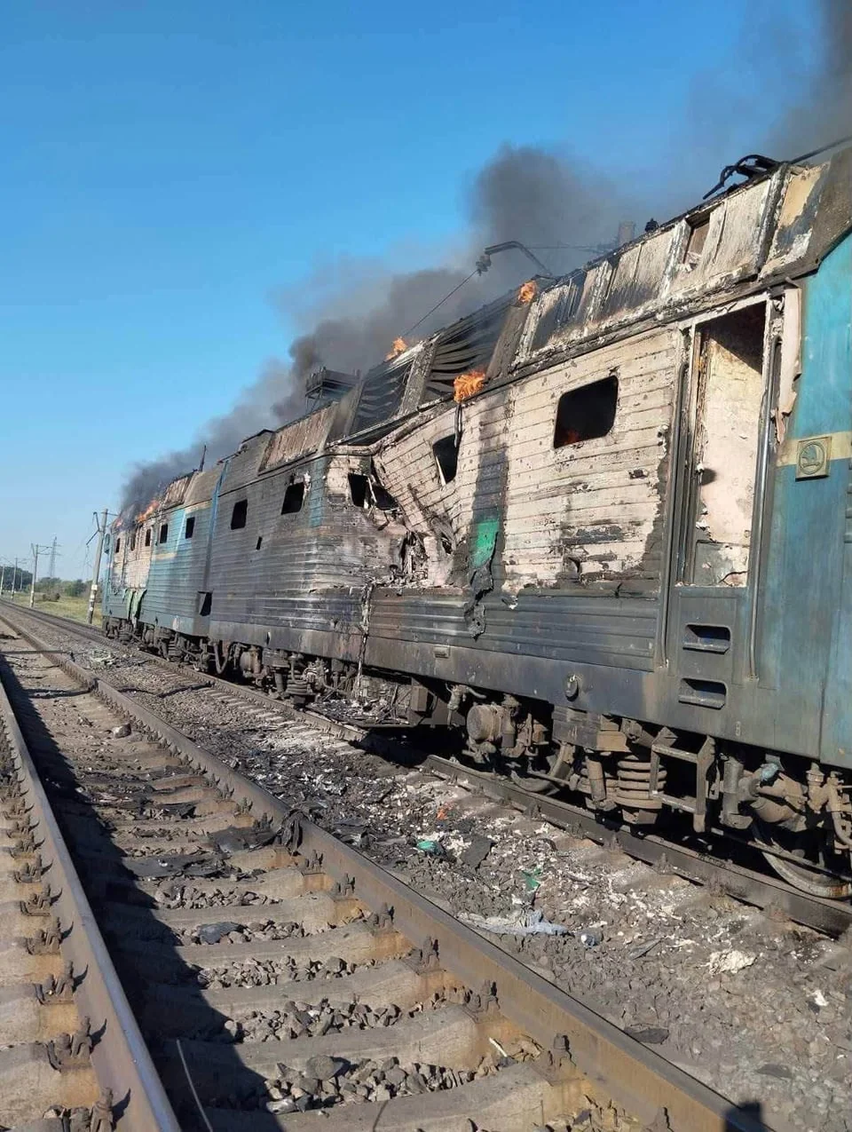 Згорілий електропоїзд на коліях із димом, полум’ям і уламками